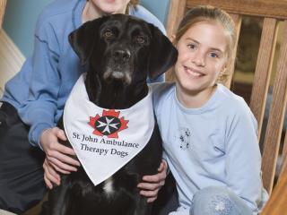 Girl and boy on stairs posing with St. John Ambulance therapy dog.